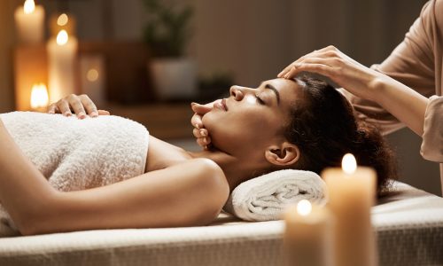 Attractive african girl enjoying face massage in spa salon. Closed eyes.